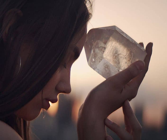 A picture of a lady holding a clear quartz crystal to her forehead and meditating